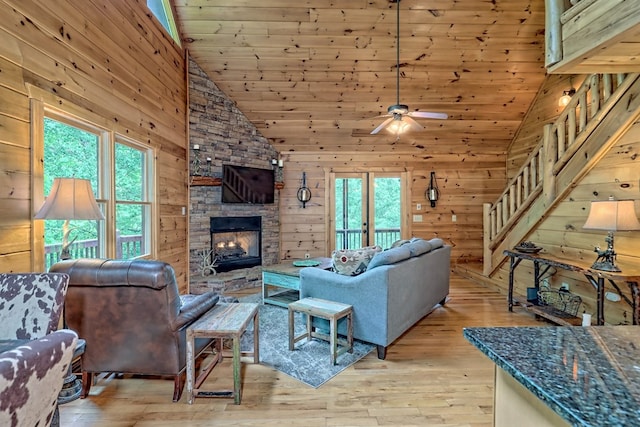 living room featuring high vaulted ceiling, light hardwood / wood-style floors, wooden walls, a fireplace, and wood ceiling