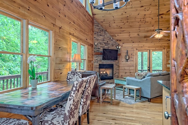 dining room featuring a stone fireplace, wood walls, high vaulted ceiling, and light wood-type flooring