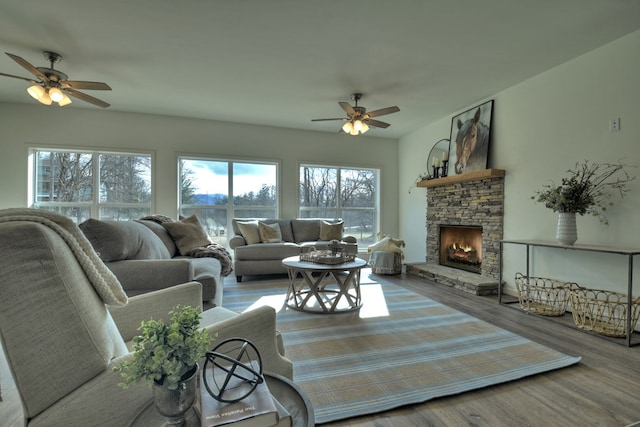 living room featuring a stone fireplace, hardwood / wood-style floors, and ceiling fan