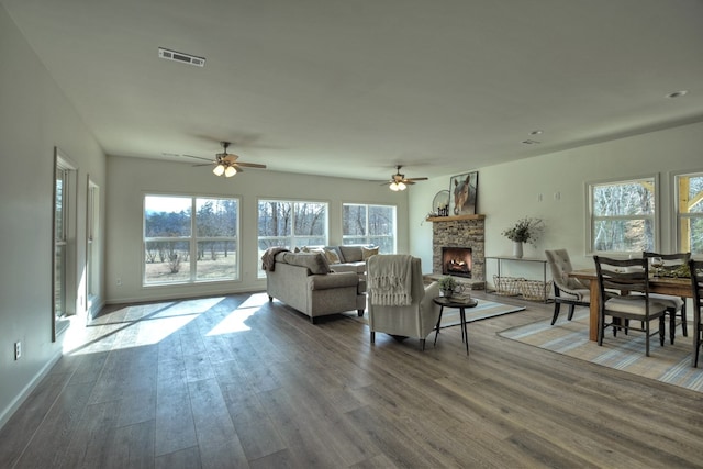 living room featuring dark hardwood / wood-style floors, ceiling fan, plenty of natural light, and a stone fireplace