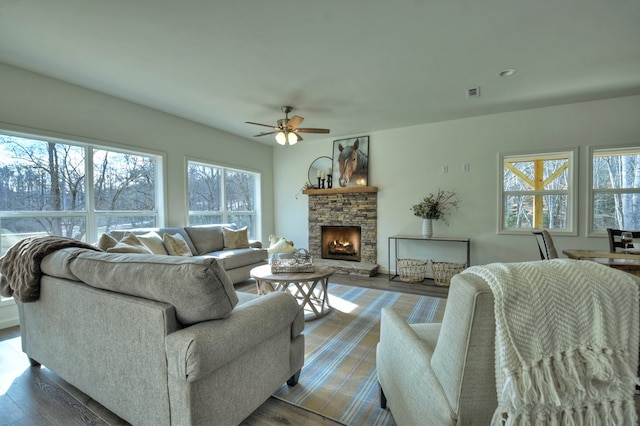 living room with wood-type flooring, a stone fireplace, and ceiling fan