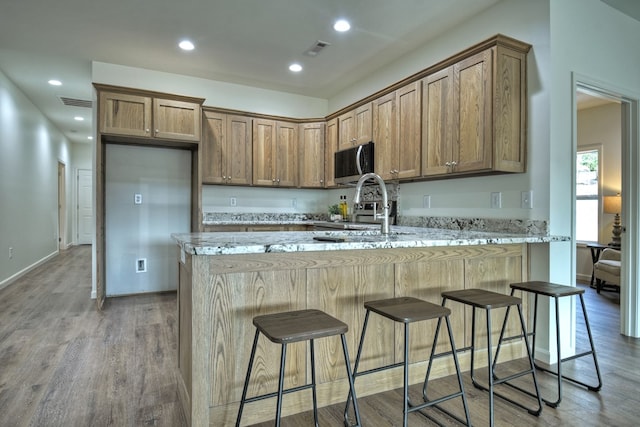 kitchen with sink, light stone countertops, hardwood / wood-style floors, and a kitchen bar