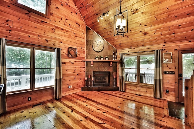 unfurnished living room featuring hardwood / wood-style flooring, wood walls, high vaulted ceiling, a tiled fireplace, and wood ceiling
