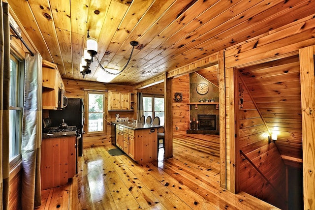 kitchen with wood ceiling, light wood-type flooring, dark countertops, wood walls, and stainless steel microwave