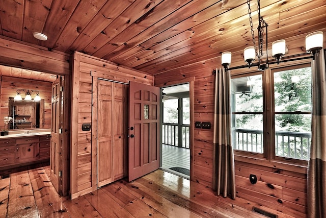 doorway to outside with wooden walls, light wood-style floors, a chandelier, wooden ceiling, and a sink