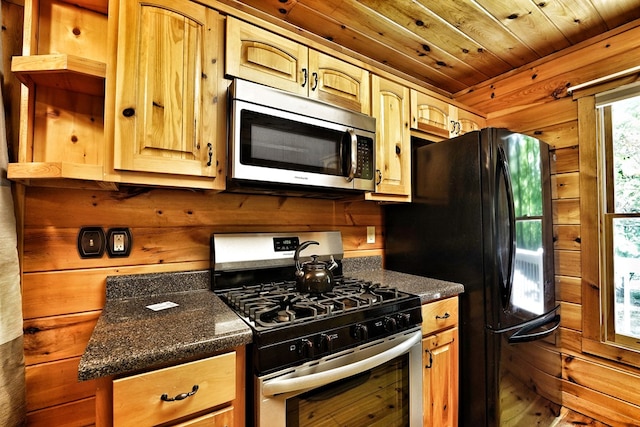 kitchen featuring stainless steel appliances, wood walls, and dark stone counters