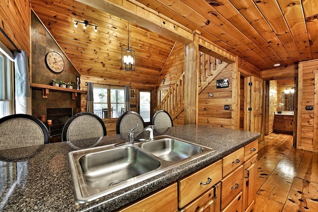 kitchen with a sink, wooden ceiling, wood-type flooring, a tiled fireplace, and wood walls