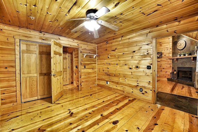 spare room featuring light wood-style flooring, wood walls, a ceiling fan, wooden ceiling, and a fireplace