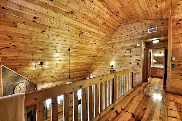 corridor with wood walls, wood ceiling, vaulted ceiling, hardwood / wood-style floors, and an upstairs landing