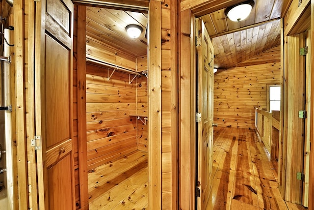 corridor with vaulted ceiling, wooden walls, light wood finished floors, and wood ceiling