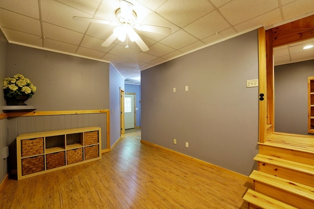 empty room with ceiling fan, wood finished floors, a drop ceiling, and stairway