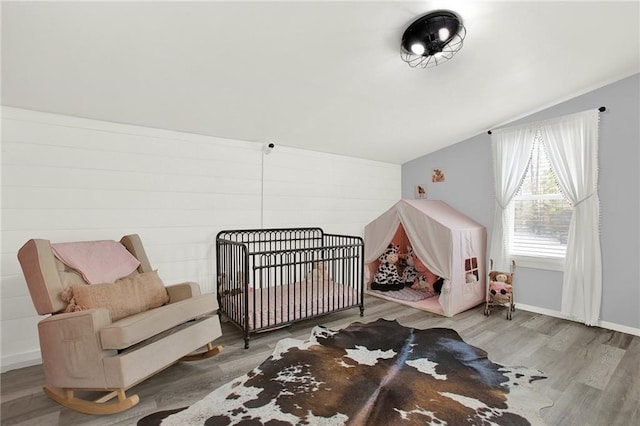 bedroom featuring wood-type flooring, vaulted ceiling, and a crib