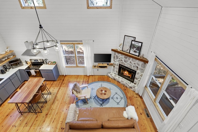 living room featuring a towering ceiling, wooden walls, light hardwood / wood-style flooring, a notable chandelier, and a stone fireplace