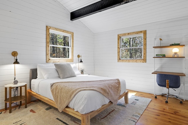 bedroom with vaulted ceiling with beams, light hardwood / wood-style floors, wooden walls, and multiple windows