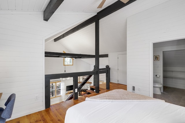 bedroom with wooden walls, lofted ceiling with beams, wood-type flooring, and connected bathroom