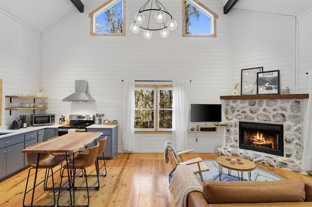 interior space featuring beamed ceiling, wall chimney range hood, stainless steel appliances, and high vaulted ceiling