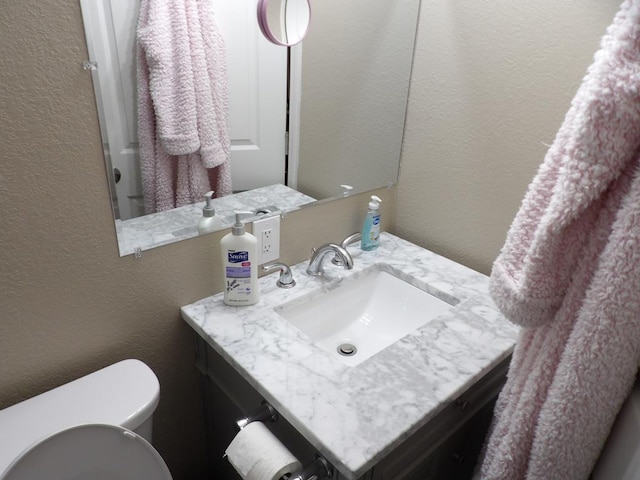 bathroom featuring toilet, vanity, and a textured wall