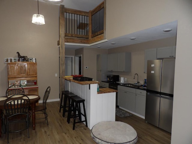 kitchen with a sink, white cabinetry, wood counters, freestanding refrigerator, and decorative light fixtures