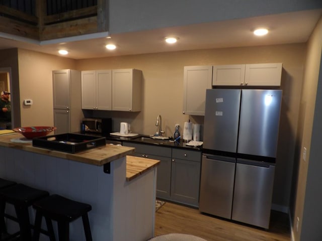 kitchen with a breakfast bar area, stainless steel appliances, gray cabinets, a sink, and butcher block countertops