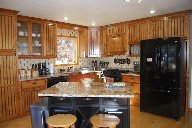 kitchen featuring black appliances, custom exhaust hood, brown cabinetry, and light wood-style floors