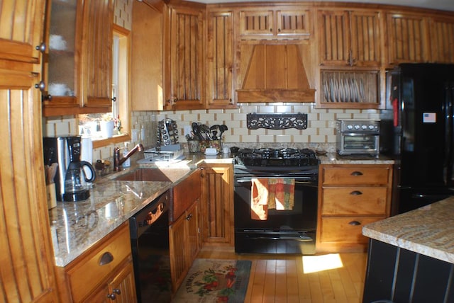 kitchen with a sink, black appliances, brown cabinetry, and custom range hood