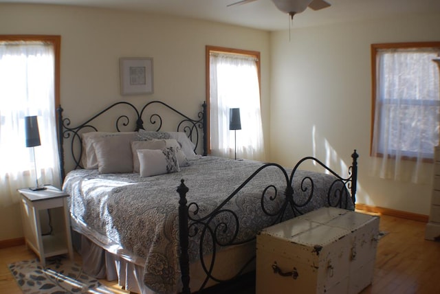 bedroom featuring multiple windows, baseboards, and light wood-style floors