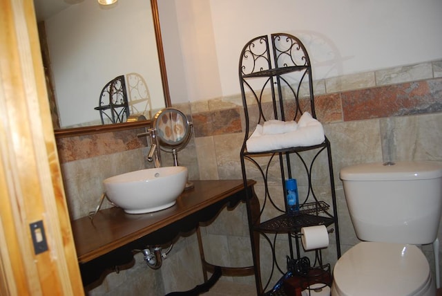 half bath featuring toilet, tile walls, and a sink