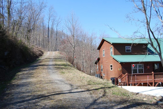 view of side of home with faux log siding, cooling unit, metal roof, and dirt driveway