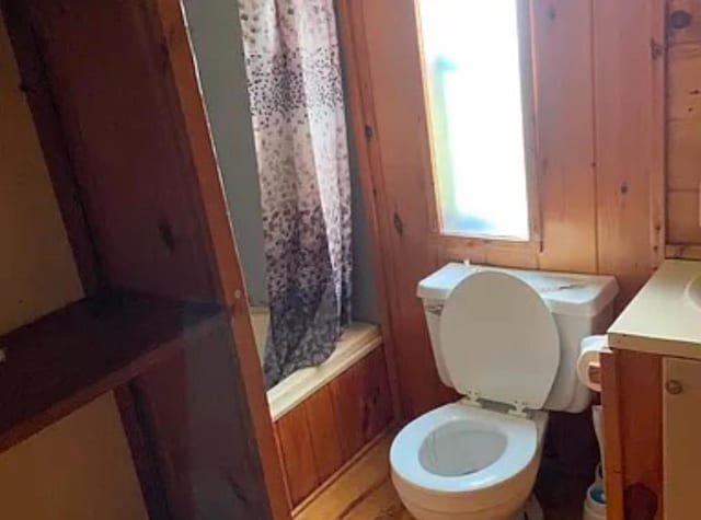 full bathroom featuring wood walls, vanity, shower / bath combination with curtain, and toilet