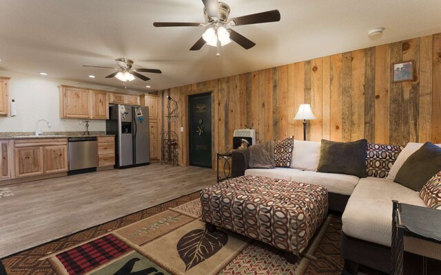 living room featuring wood walls, sink, ceiling fan, and light wood-type flooring