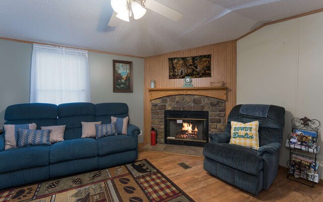 living room featuring lofted ceiling, light wood-type flooring, a textured ceiling, ceiling fan, and a fireplace