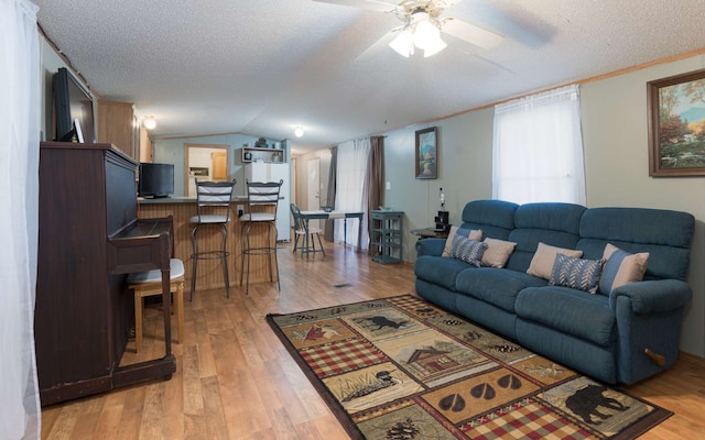 living room with ceiling fan, lofted ceiling, light wood-type flooring, and a textured ceiling