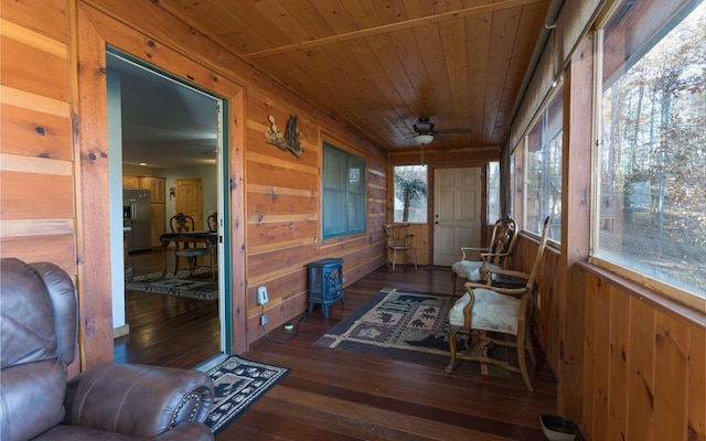 sunroom / solarium with wooden ceiling, ceiling fan, and a wood stove