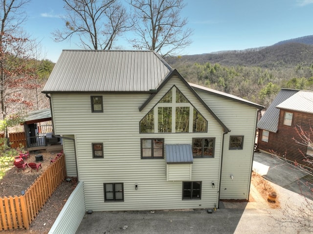 back of property with a mountain view, metal roof, and fence