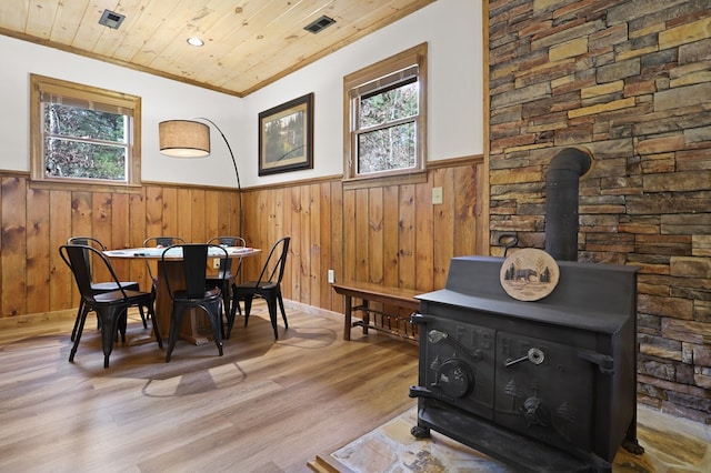 dining area with a wood stove, wooden ceiling, crown molding, wooden walls, and light wood-type flooring