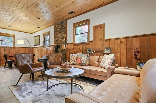 living room with light hardwood / wood-style floors, wood ceiling, wooden walls, and a wood stove