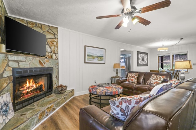 living room featuring a textured ceiling, ceiling fan, wooden walls, wood-type flooring, and a fireplace