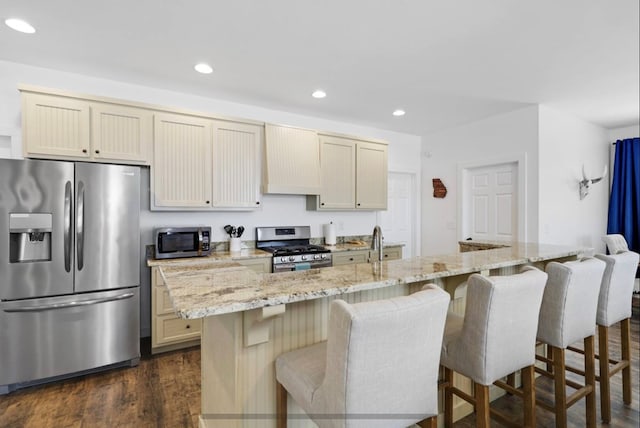 kitchen with a breakfast bar, a center island with sink, light stone counters, appliances with stainless steel finishes, and dark hardwood / wood-style flooring