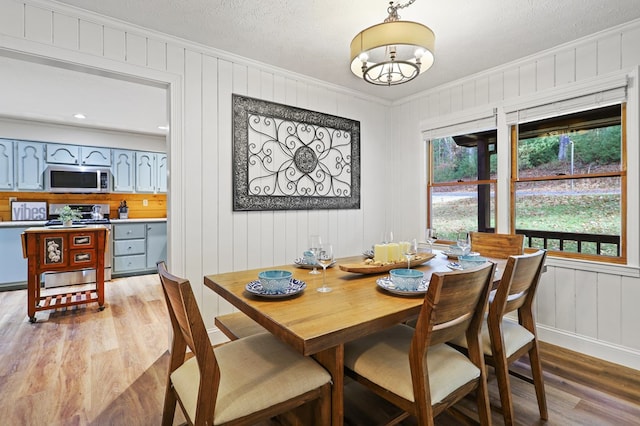 dining room featuring a chandelier, crown molding, light hardwood / wood-style floors, and a textured ceiling