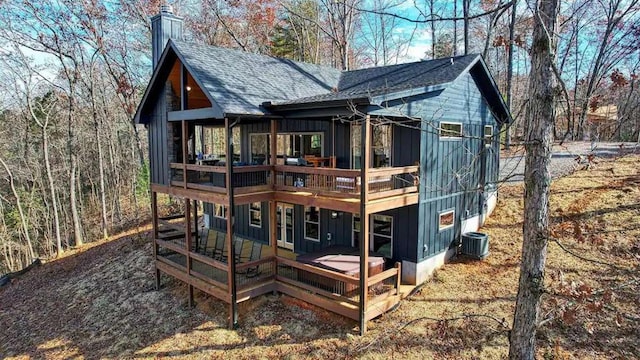 rear view of property with a deck, central AC, a shingled roof, board and batten siding, and a chimney