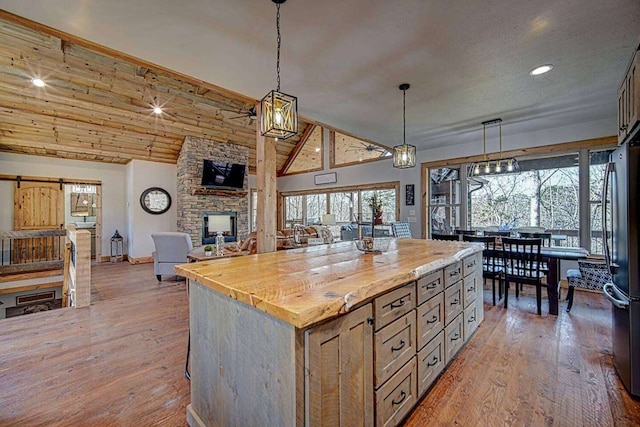 kitchen with a stone fireplace, open floor plan, wooden counters, light wood-type flooring, and freestanding refrigerator