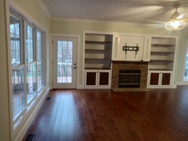 unfurnished living room featuring a fireplace, crown molding, built in shelves, and dark hardwood / wood-style floors