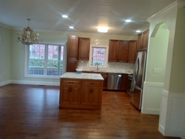 kitchen with appliances with stainless steel finishes, crown molding, a kitchen island, and dark wood-type flooring