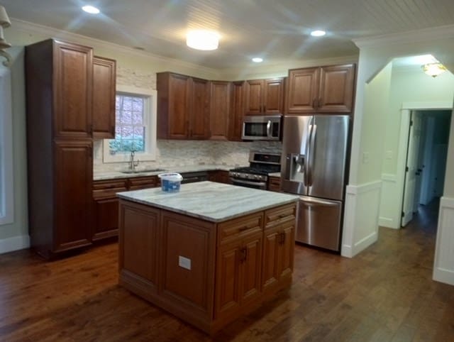 kitchen featuring backsplash, a center island, stainless steel appliances, dark wood-type flooring, and ornamental molding