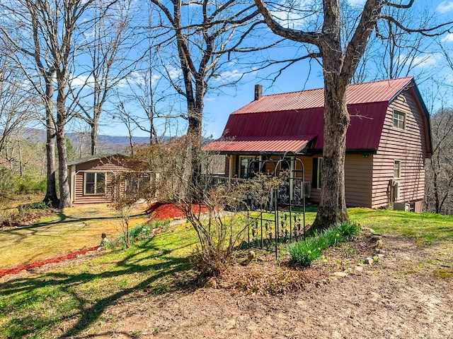 view of front of property featuring a gambrel roof, metal roof, covered porch, and a front yard