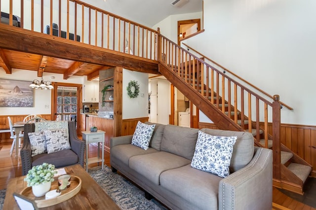 living room with stairs, wainscoting, wood finished floors, a chandelier, and wooden walls