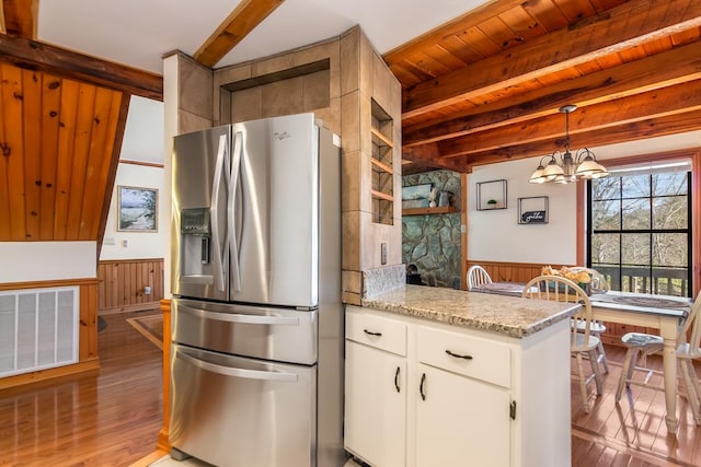 kitchen with stainless steel fridge, light wood-style flooring, beamed ceiling, a wainscoted wall, and wood walls
