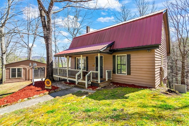 view of front facade with covered porch, an outbuilding, a front lawn, and metal roof