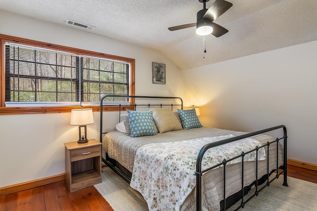 bedroom featuring baseboards, wood-type flooring, a textured ceiling, lofted ceiling, and a ceiling fan
