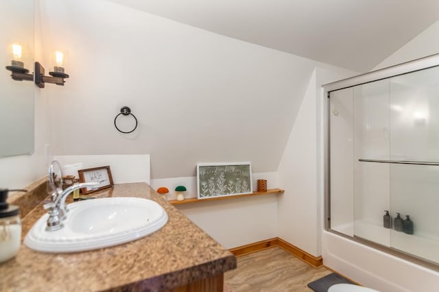 full bathroom with lofted ceiling, bath / shower combo with glass door, vanity, wood finished floors, and baseboards